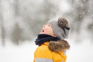 Pieni lapsi keltaisessa talvitakissa ihailee taivaalta satavaa lunta.